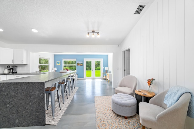 kitchen featuring a kitchen breakfast bar, white cabinetry, a textured ceiling, french doors, and sink