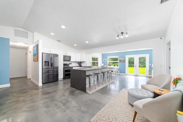 kitchen featuring white cabinets, a breakfast bar area, appliances with stainless steel finishes, a textured ceiling, and vaulted ceiling