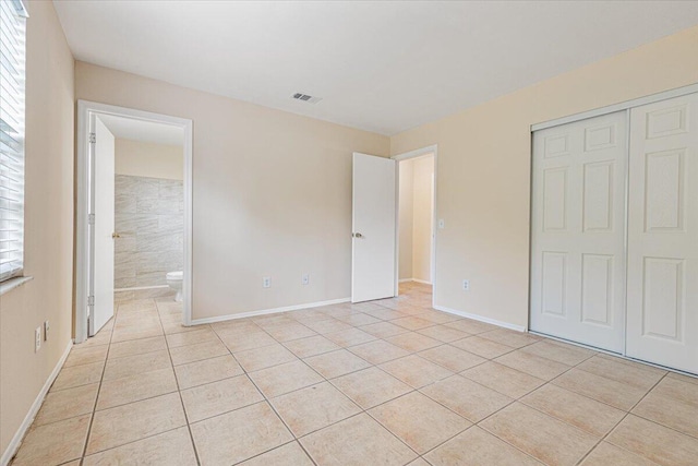 unfurnished bedroom with a closet, connected bathroom, and light tile patterned flooring