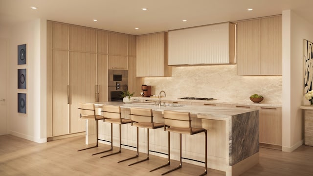 kitchen featuring sink, light brown cabinets, light hardwood / wood-style flooring, backsplash, and a kitchen island with sink