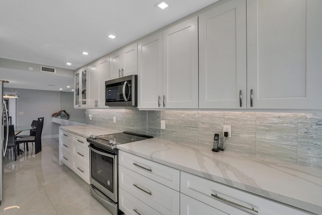 kitchen with light stone countertops, light tile patterned floors, backsplash, white cabinets, and appliances with stainless steel finishes