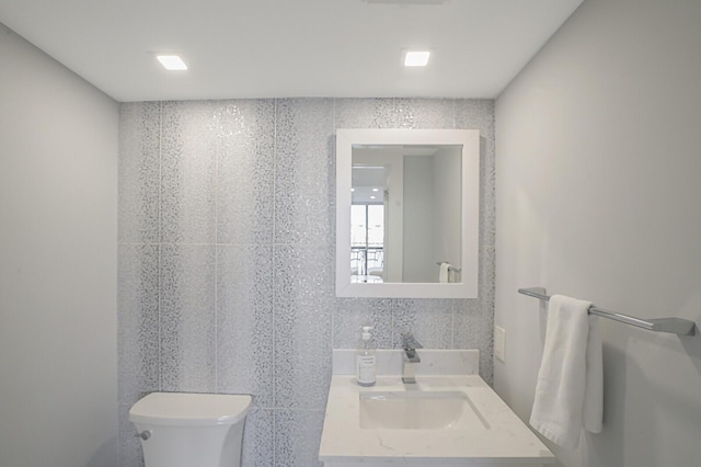 bathroom with toilet, tile walls, and sink