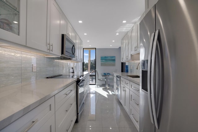 kitchen featuring white cabinetry, sink, light stone countertops, decorative backsplash, and appliances with stainless steel finishes