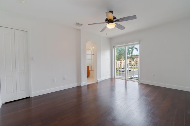 spare room featuring visible vents, baseboards, ceiling fan, dark wood-type flooring, and arched walkways