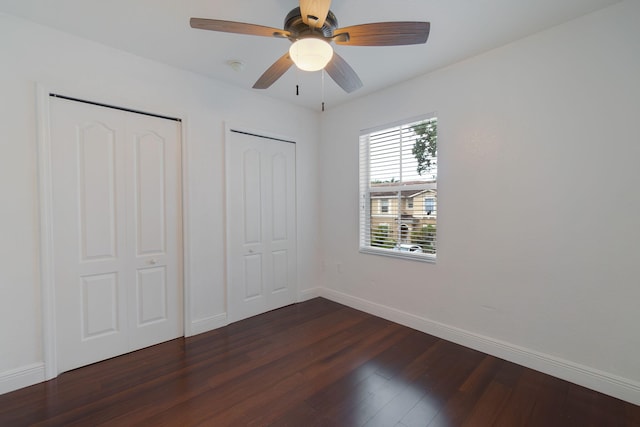 unfurnished bedroom with a ceiling fan, baseboards, multiple closets, and dark wood-style floors