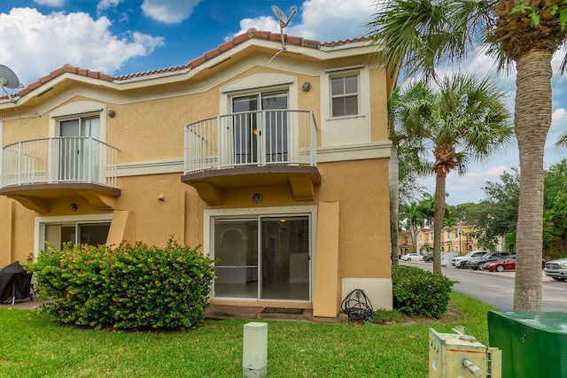 rear view of property featuring a lawn, stucco siding, a tile roof, and a balcony