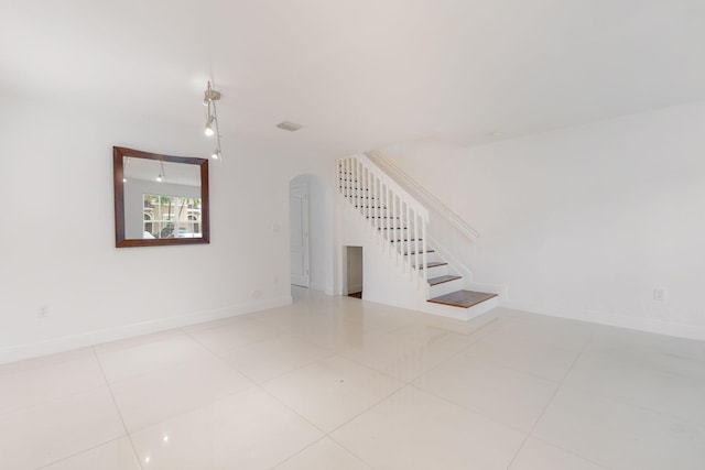 unfurnished living room with tile patterned flooring, arched walkways, baseboards, visible vents, and stairway