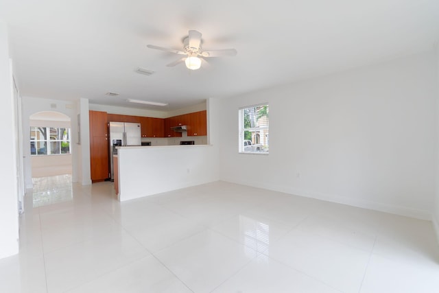 unfurnished living room featuring visible vents, a ceiling fan, baseboards, and arched walkways