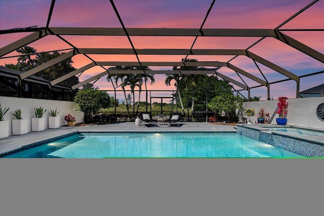 pool at dusk with an in ground hot tub, a patio, and glass enclosure