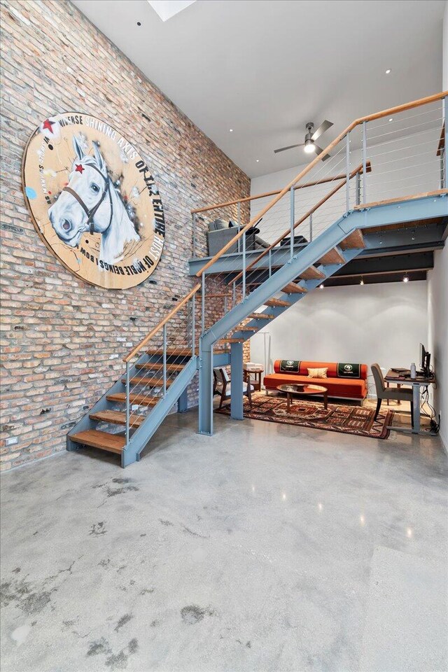 stairs featuring ceiling fan and brick wall