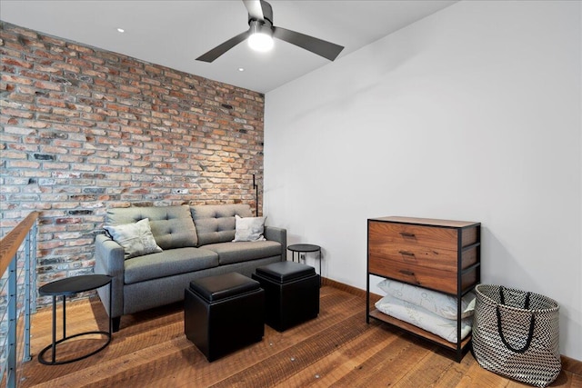 living room featuring hardwood / wood-style floors, ceiling fan, and brick wall