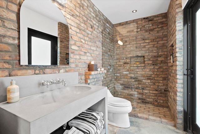 bathroom featuring vanity, toilet, and brick wall