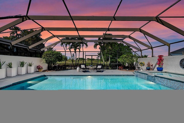 pool at dusk featuring an in ground hot tub, a patio, and glass enclosure