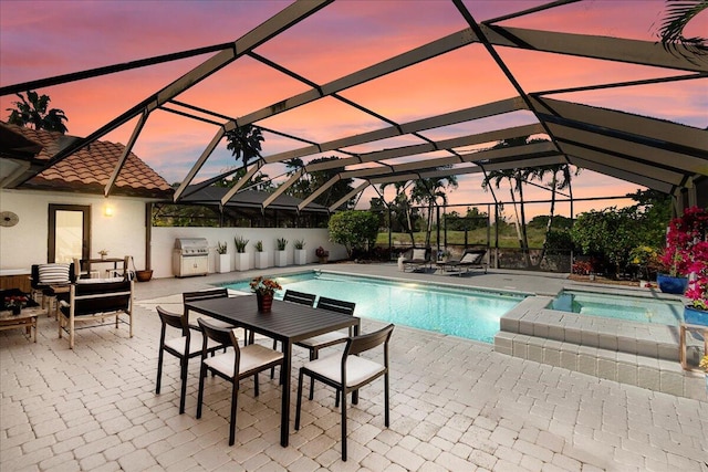 pool at dusk with an in ground hot tub, area for grilling, a lanai, and a patio area