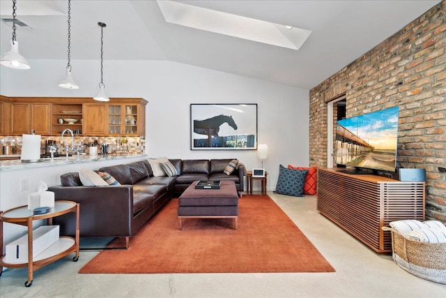 carpeted living room featuring vaulted ceiling with skylight, sink, and brick wall