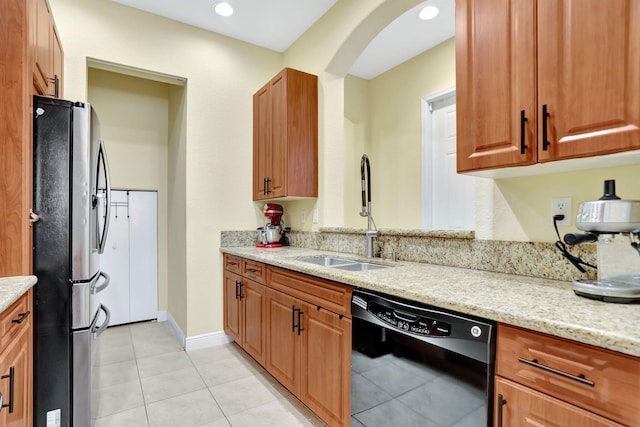 kitchen with black dishwasher, light stone countertops, sink, and stainless steel fridge