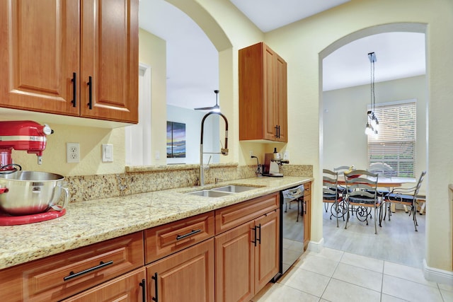 kitchen featuring sink, dishwasher, hanging light fixtures, light stone counters, and light tile patterned floors