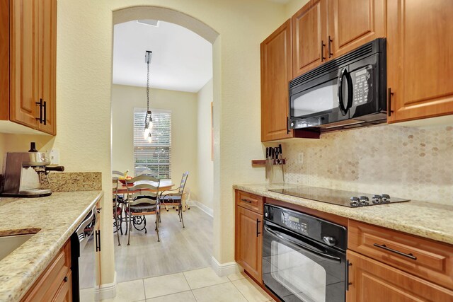 kitchen featuring light stone counters, black appliances, hanging light fixtures, and tasteful backsplash