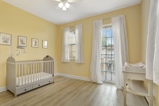 bedroom with light hardwood / wood-style flooring, multiple windows, a crib, and ceiling fan