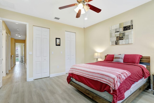 bedroom featuring light hardwood / wood-style flooring, multiple closets, and ceiling fan