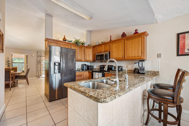 kitchen featuring a textured ceiling, kitchen peninsula, stainless steel appliances, dark stone counters, and vaulted ceiling