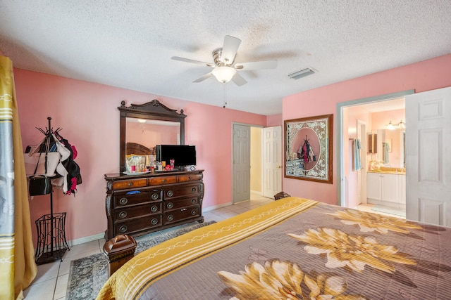 bedroom with a textured ceiling, ensuite bathroom, light tile patterned floors, and ceiling fan