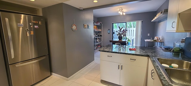 kitchen with kitchen peninsula, white cabinets, light tile patterned floors, stainless steel refrigerator, and sink