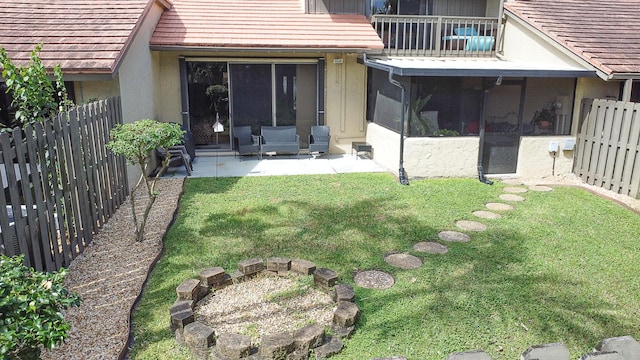 rear view of property with stucco siding, a sunroom, a fenced backyard, a patio area, and a lawn
