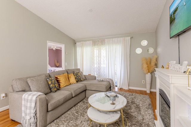 living room featuring light hardwood / wood-style flooring, a textured ceiling, ceiling fan, and vaulted ceiling