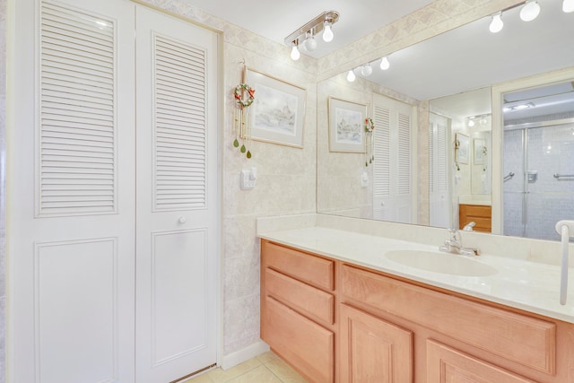 bathroom with a shower with door, vanity, tile walls, and tile patterned flooring