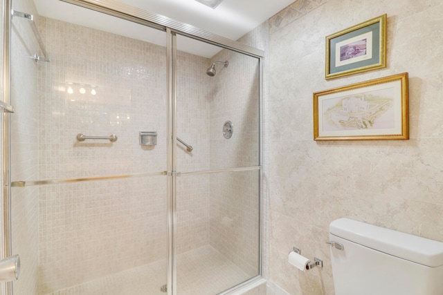 bathroom featuring toilet, tile walls, and a shower with shower door