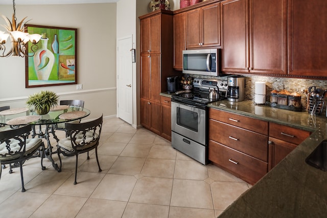 kitchen with tasteful backsplash, appliances with stainless steel finishes, light tile patterned flooring, dark stone countertops, and a chandelier