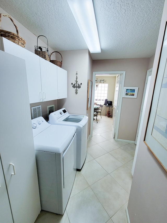 washroom featuring cabinets, a textured ceiling, washer and clothes dryer, and light tile patterned floors