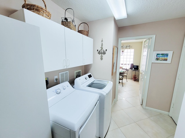 laundry area featuring a textured ceiling, light tile patterned flooring, washing machine and dryer, and cabinets