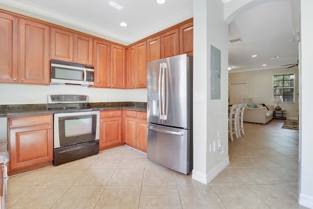 kitchen with ceiling fan, stainless steel appliances, dark stone countertops, crown molding, and light tile patterned floors