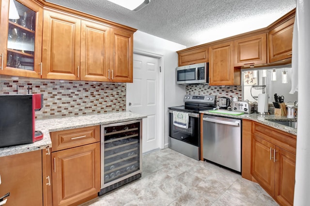 kitchen featuring appliances with stainless steel finishes, wine cooler, light stone countertops, and backsplash