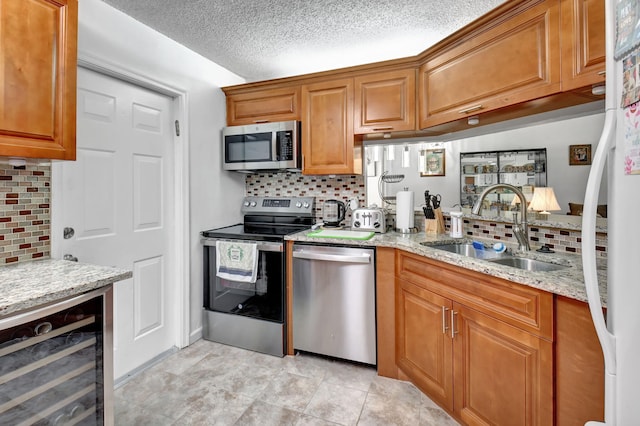 kitchen with decorative backsplash, wine cooler, appliances with stainless steel finishes, light stone countertops, and sink