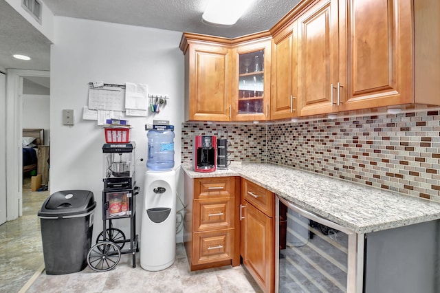 kitchen with a textured ceiling, light stone countertops, tasteful backsplash, and beverage cooler