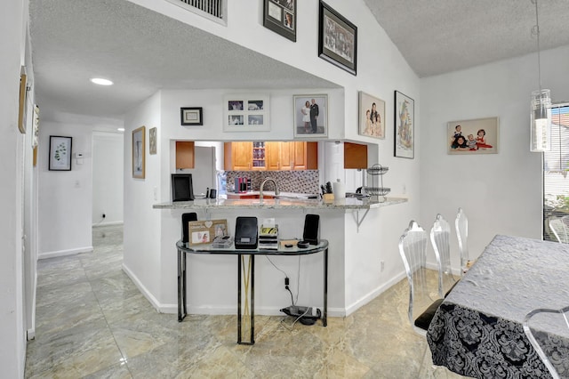 kitchen with light stone countertops, a textured ceiling, kitchen peninsula, and a kitchen breakfast bar