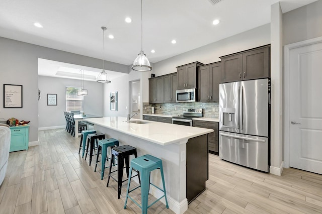 kitchen with light wood-type flooring, stainless steel appliances, pendant lighting, a breakfast bar, and a kitchen island with sink