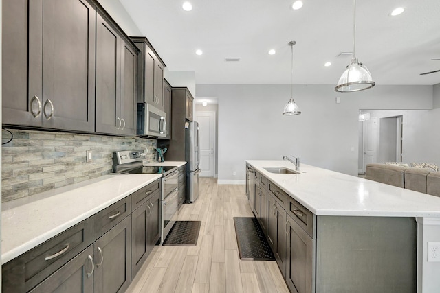 kitchen featuring sink, light wood-type flooring, hanging light fixtures, stainless steel appliances, and a center island with sink