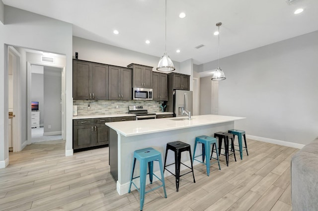 kitchen with hanging light fixtures, an island with sink, a breakfast bar, light hardwood / wood-style flooring, and stainless steel appliances