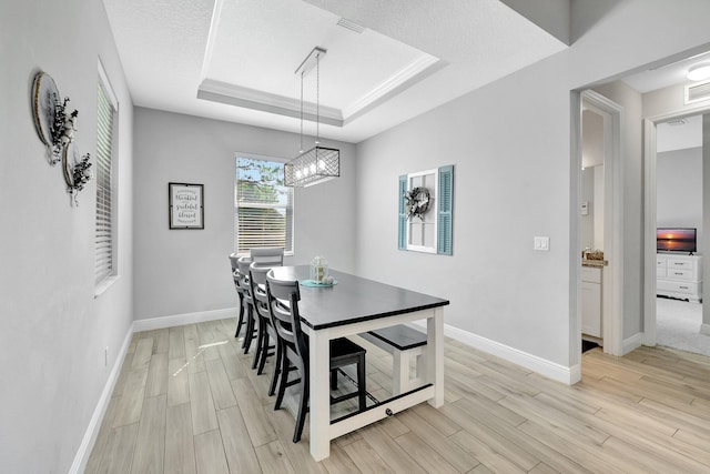 dining room with light hardwood / wood-style flooring, a textured ceiling, and a tray ceiling