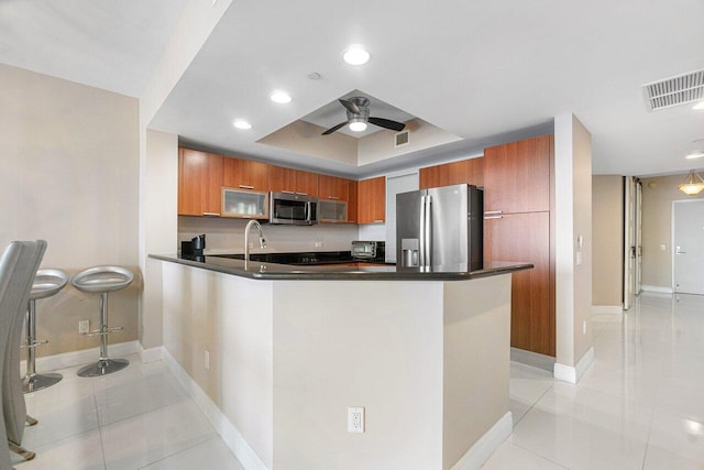 kitchen featuring kitchen peninsula, appliances with stainless steel finishes, light tile patterned floors, a tray ceiling, and ceiling fan