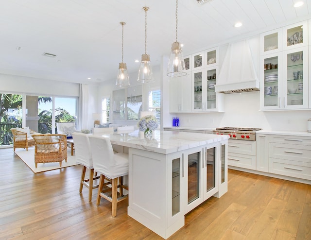 kitchen featuring stainless steel gas cooktop, white cabinets, light stone counters, a kitchen island, and custom range hood