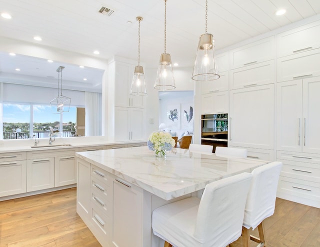 kitchen with white cabinets, a center island, light wood-type flooring, and pendant lighting