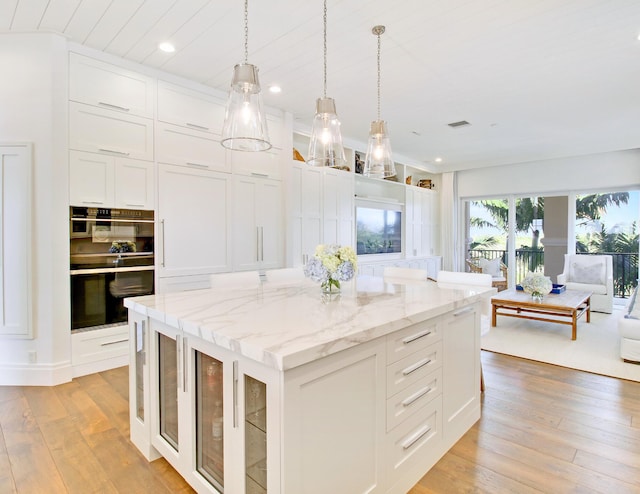 kitchen featuring light stone counters, a kitchen island, double oven, pendant lighting, and white cabinetry