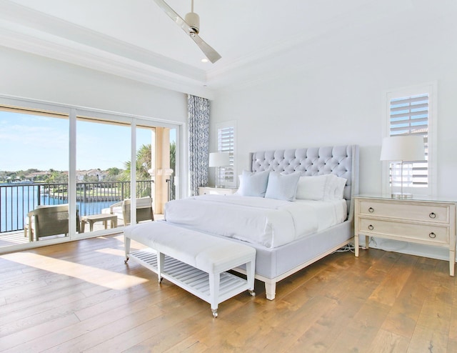 bedroom featuring access to exterior, ceiling fan, a high ceiling, a water view, and hardwood / wood-style flooring