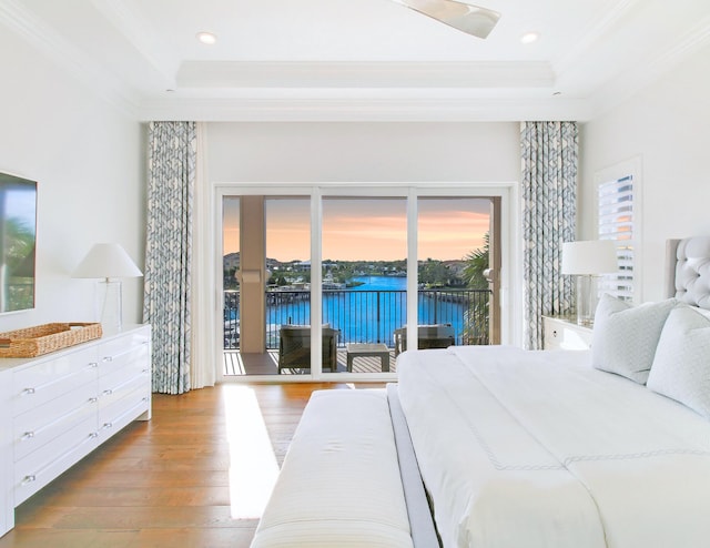 bedroom featuring access to exterior, a raised ceiling, a water view, and wood-type flooring