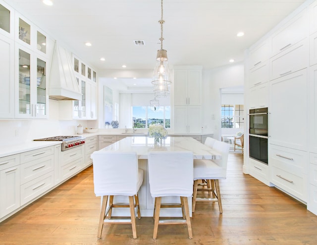 kitchen with a breakfast bar area, a center island, white cabinets, and custom exhaust hood